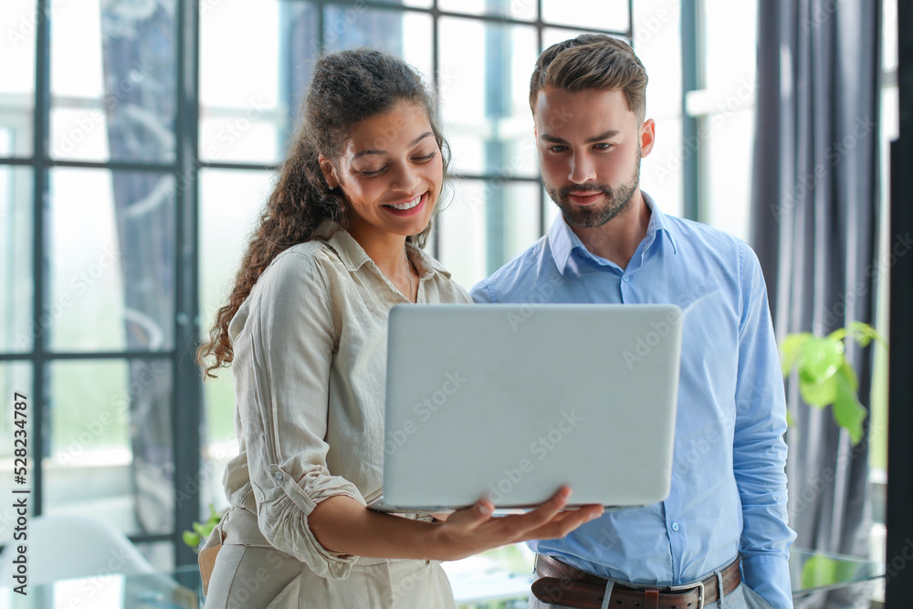 Modern business people are working using laptop and smiling while standing in the office. Modern business people are working using laptop and smiling while standing in the office.