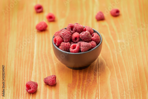 Ripe sweet raspberries in bowl on wooden table