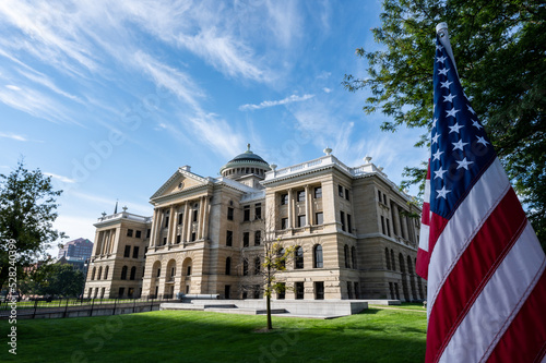 Side angle photo of Lucas county courthouse with the United States flag in the foreground in downtown Toledo Ohio