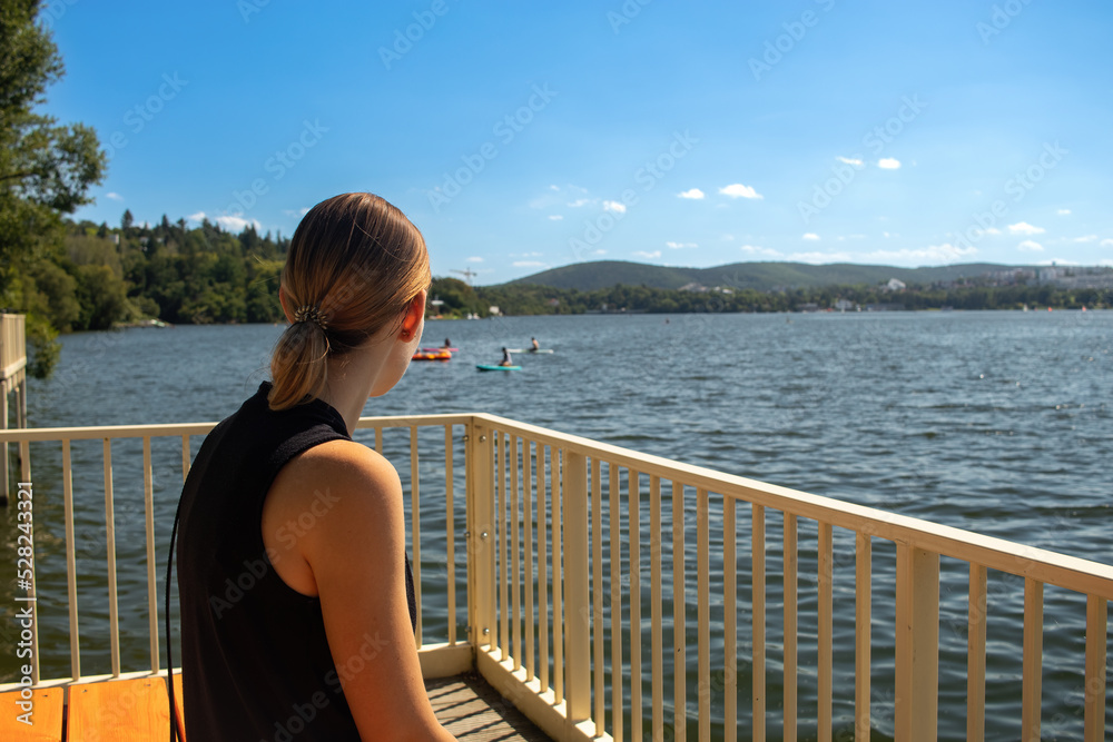Beauty of a young woman from behind sitting on a pier waiting for a ship.