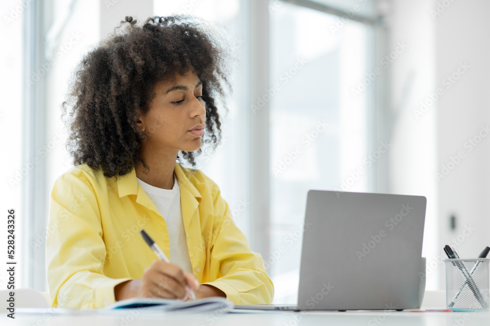 Focused millennial african american female student giving online class at home, taking notes in notebook, copy space, e-education Focused millennial african american female student giving online class at home, taking notes in notebook, copy space, e-education