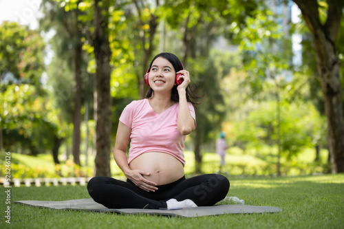 Young Asian pregnant woman enjoys listening to music with headphones in the park