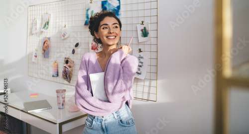 Gentle sweet girl in purple sweater posing at camera smiling sincerely from. Radiant brunette woman with beautiful appearance holds diary in hands. Positive female student with notebook organizer