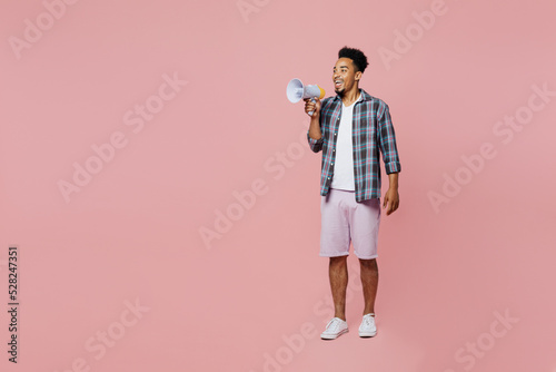 Full body young smiling man of African American ethnicity 20s wear blue shirt hold scream in megaphone announces discounts sale Hurry up isolated on plain pastel light pink background studio portrait.