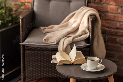 Morning coffee. Cozy interior: a cup of coffee and an open book on a table against the background of a wicker chair with a plaid. Leisure on the terrace in the garden.