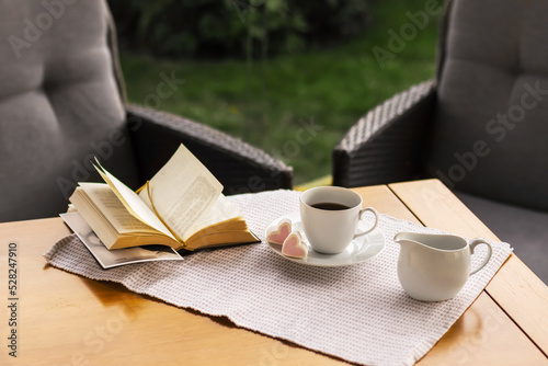 Morning coffee. Cozy interior  a cup of coffee and an open book on the table against the background of a wicker chair. Relax on the terrace in the garden.