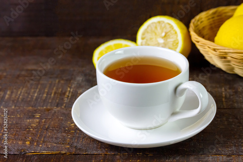 Cup of hot tea in white ceramic cup and fresh lemon on rustic wooden table.