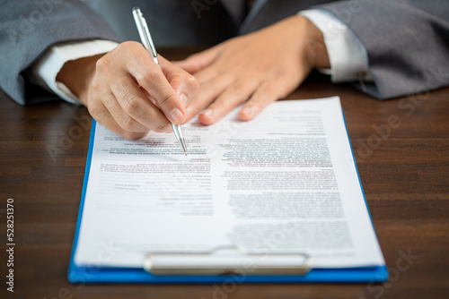 Workplace closeup person professional businesswoman sitting at desk hold pen signing or signature contract paper. Employee woman writing agreement document on paperwork form corporate at work office