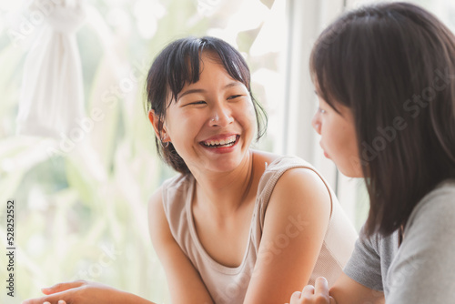 Young cheerful happy Asian university student working on laptop notebook together at coffee cafe. Attractive lesbian couple as a content creator talking sharing idea with relax moment.