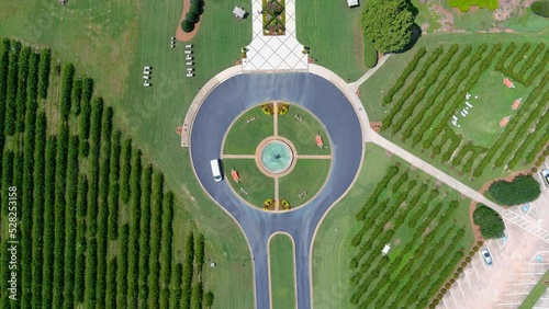 aerial footage of a circular driveway with a water fountain in the center at a vineyard surrounded by lush green trees, grass and plants at Chateau Elan Winery & Resort in Braselton Georgia USA 