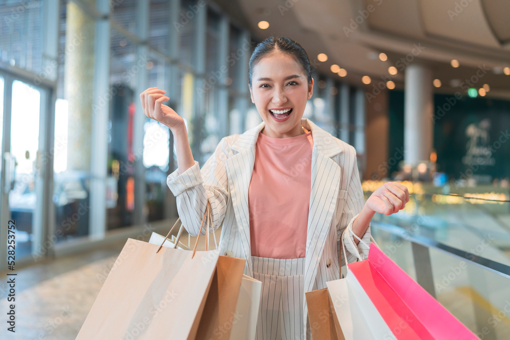 surprising cheerful asian female adult woman shopper hand hold shopping bag happiness lifestyle walking buying cloths in department store shopping mall with happiness exited toothy smiling joyful