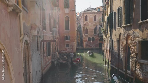 Gimbal shot of two gondolas in narrow canal among old houses. Venice, Italy. Typical Venetian canal with gondolas early in the morning