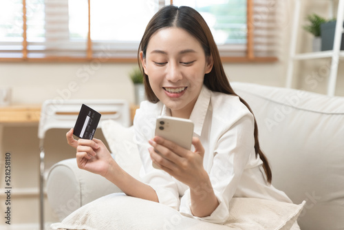 Happy Asian young woman using mobile phone shopping online and pay via credit card to get cashback bonus.