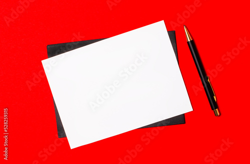 Black pen, envelope and white blank card with space to insert text on a bright red background