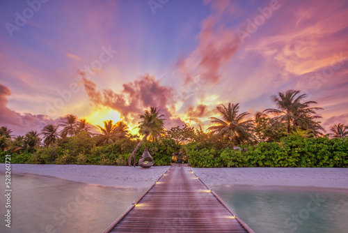 Beautiful panoramic sunset tropical paradise beach. Tranquil summer vacation or holiday landscape. Wooden pier pathway seaside palm calm sea, lights exotic nature view inspirational seascape scenic