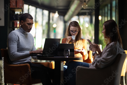 Three multiracial business colleagues having a meeting after work or during coffee break in a restaurant. Friends working at a cafe bar..