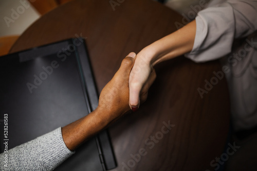 Two multiracial business colleagues working after work or during coffee break in a restaurant. Man and woman shaking hands after successful meeting..