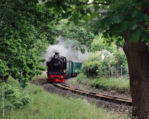 old steam train rides in greenery and blows a lot of smoke