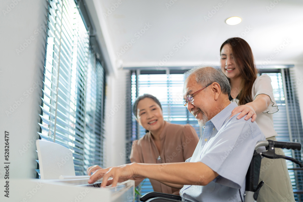 Elderly retirement father sitting on wheel chair playing piano and wife looking at his face in the living room. Daughter caregiver take care senior family. Home health care and enjoying on holiday