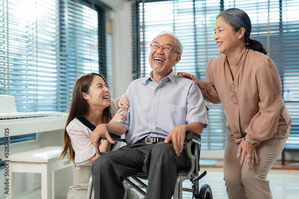 Elderly retirement father laugh and happy sitting on wheel chair with his wife and daughter. Daughter caregiver take care senior family. Home health care and enjoying on holiday. Family lifestyle