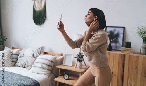 Fotografie, Obraz Stylish Hispanic female blogger taking selfie on smartphone at home