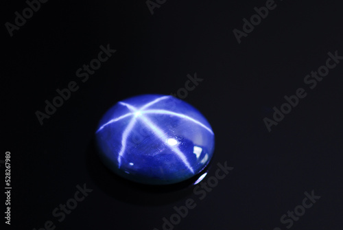 Natural rich blue star sapphire cabochone oval loose gemstone setting for making jewelry. Black background isolated. Diffusion treated, heated, color enhanced gem. Gemology, mineralogy. Close up.
