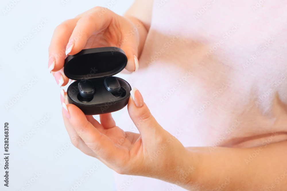 Woman with wireless headphones. Close up of woman is holding the black wireless earbuds case in hand Woman with wireless headphones. Close up of woman is holding the black wireless earbuds case in hand
