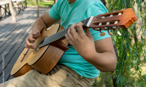 The young man plays hands and on a classic acoustic wooden guitar on the street. Focus close-up shot of teenage boy hand playing strings of an acoustic guitar.