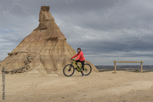 Fotografie Young woman mountain bike cyclist next to Castildetierra Mountain in Badlans of Navarre (Bardenas Reales de Navarra) dessert in the middle of Spain