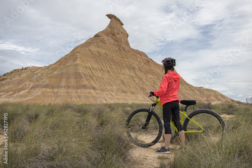 Fotografie Young woman mountain bike cyclist in Badlans of Navarre (Bardenas Reales de Navarra) dessert in the middle of Spain