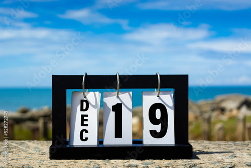 Dec 19 calendar date text on wooden frame with blurred background of ocean.