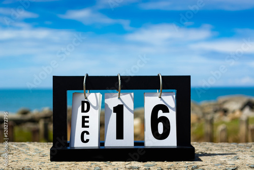 Dec 16 calendar date text on wooden frame with blurred background of ocean.