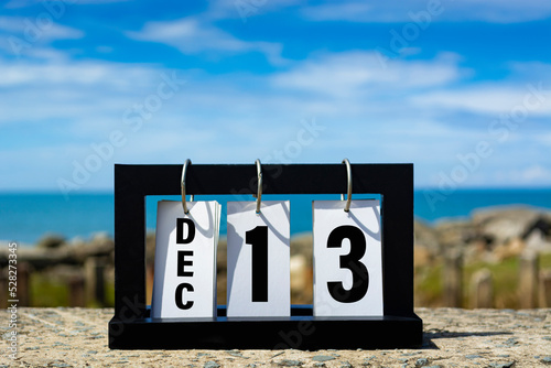 Dec 13 calendar date text on wooden frame with blurred background of ocean.
