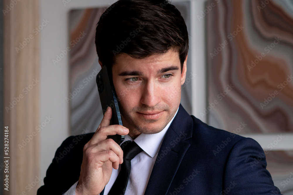 young businessman in a dark blue suit working in the office, talking by mobile phone young businessman in a dark blue suit working in the office, talking by mobile phone