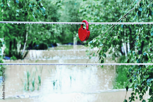 A small lock in the form of a wedding heart on a rope near the water of the river