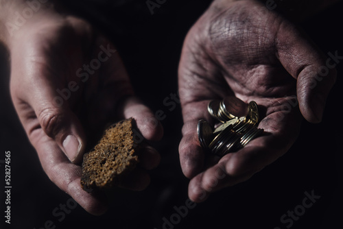 Hungry man holding money and bread on a black background, hands with food close-up. Cash in the dirty hands of a starving poor man on a dark background