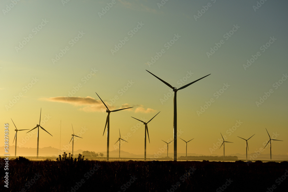 A wind farm of eerie looking turbines in a sunrise with small clouds scattered about