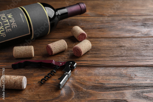 Corkscrew, wine bottle and stoppers on wooden table. Space for text