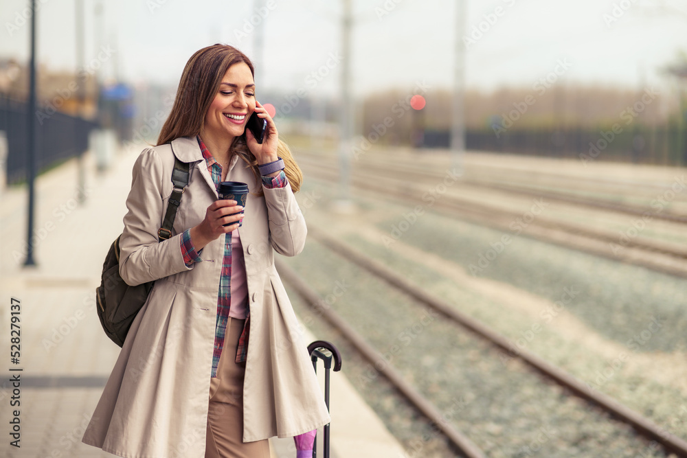 A beautiful woman in her 30s is using a mobile phone while waiting for a train at a train station.