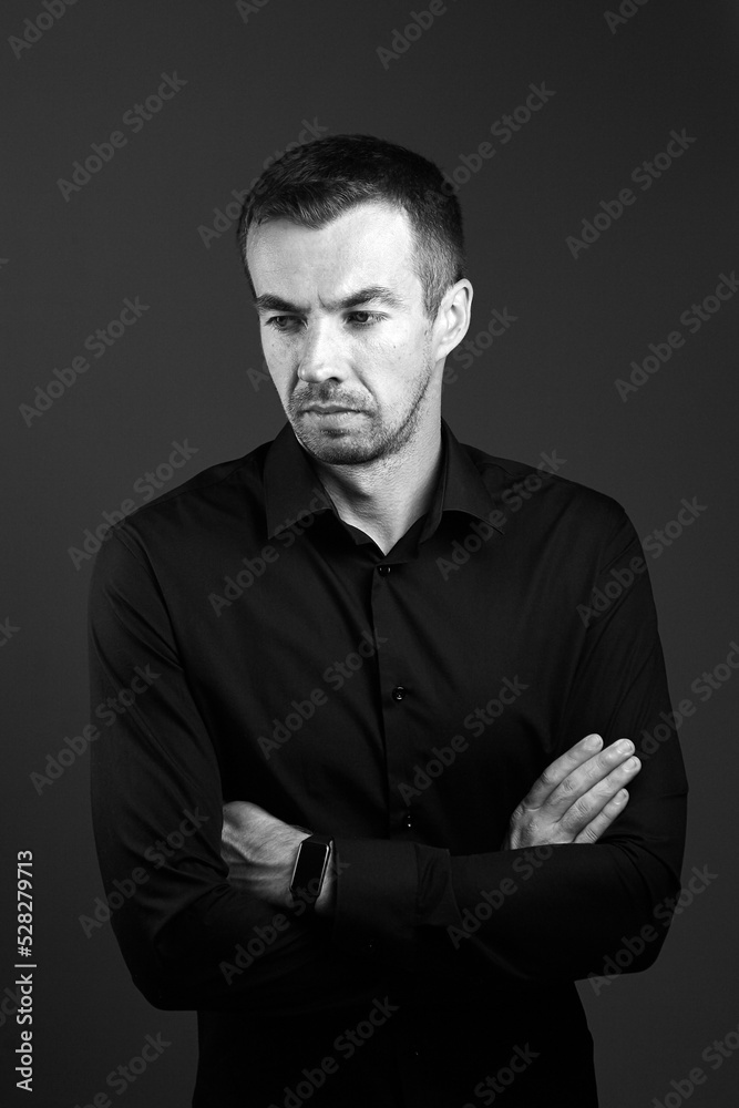 Young man portrait in a shirt on a black background. Serious businessman with arms folded