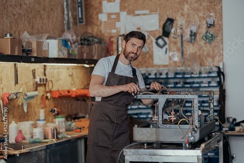 Portrait of repairman in uniform with broken coffee machine in workshop