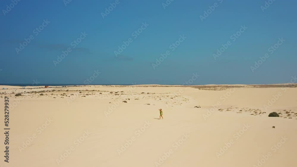 Aerial flight over white sand dunes in the desert. Natural Park, town Corralejo. Fuerteventura, Canary Islands, Spain. Cinematic. Turquoise ocean, blue sky. Girl walking enjoying vacation. Aerial flight over white sand dunes in the desert. Natural Park, town Corralejo. Fuerteventura, Canary Islands, Spain. Cinematic. Turquoise ocean, blue sky. Girl walking enjoying vacation.