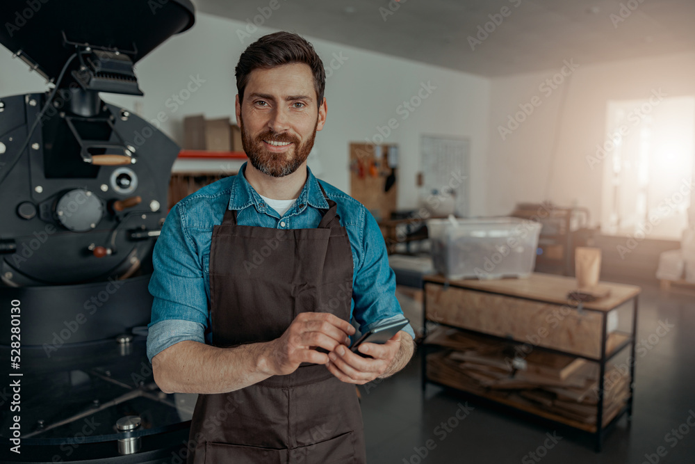 Business owner of coffee factory using phone on background of coffee roasting machine Business owner of coffee factory using phone on background of coffee roasting machine