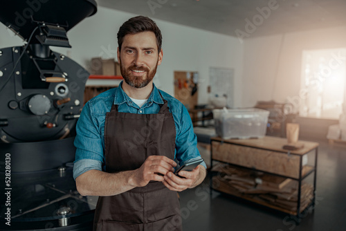 Business owner of coffee factory using phone on background of coffee roasting machine