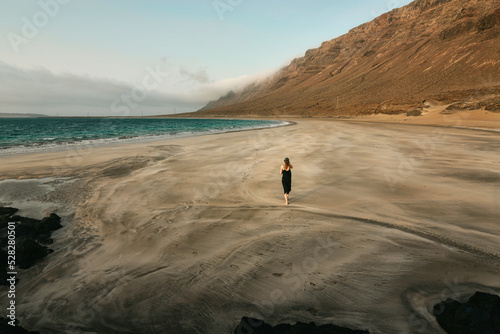 Beautiful coastal scenery with girl in black dress walking on sandy beach Del Risco at Lanzerote, Canary Islands, Spain 