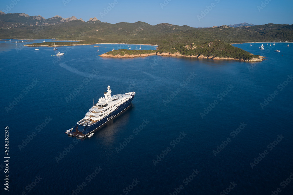 White blue mega yacht anchored off the coast of sardinia aerial view. One of the largest yachts on dark blue water in the background is the coastline top view. Mega yacht on blue water aerial view.
