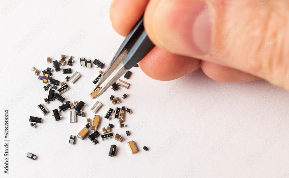 Hand with tweezers over the various micro electronic elements on white background. Hand with tweezers over the various micro electronic elements on white background.