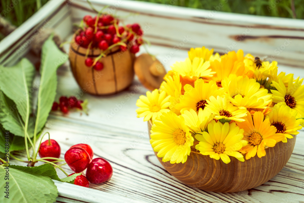 calendula flowers in a wooden bowl, red currants and cherries on a white tray in the garden calendula flowers in a wooden bowl, red currants and cherries on a white tray in the garden