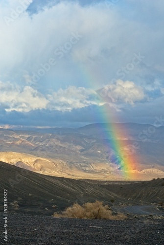 Rainbow arching over road to Ubehebe Crater with distant badlands photo