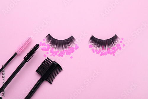 Fototapeta Naklejka Na Ścianę i Meble -  Flat lay composition with false eyelashes, confetti, makeup and mascara brushes on pink background